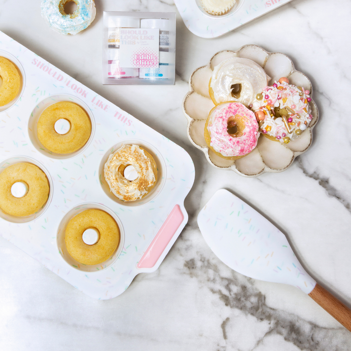 donut pan, spatula, edible glitter, and donuts displayed on countertop